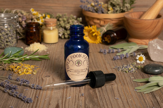 Blue bottle with dropper labeled 'Triple Moon Apothecary' on a green background